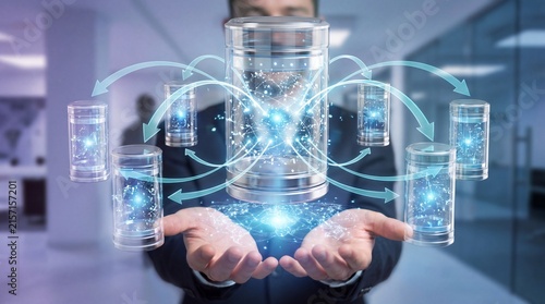 A businessman in a suit holding a glowing blue cylinder with smaller cylinders surrounding it in an office setting.
