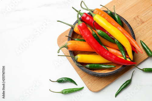 Fotografie Colorful chili peppers and bowl on light table, flat lay