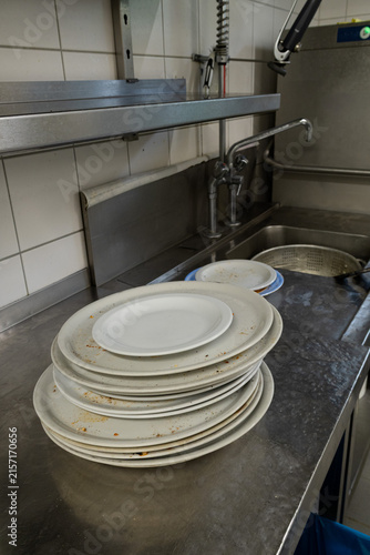 Dirty dishes stacked on sink counter in commercial kitchen during dishwashing service