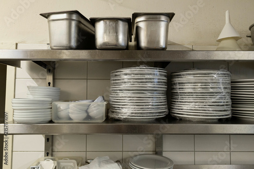 Organized kitchen storage shelves with metal pots plates and containers in commercial restaurant