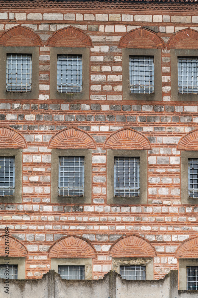 Obraz premium Red brick wall with arched windows and metal grilles