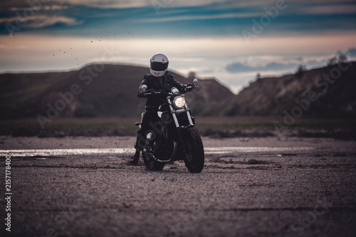 Motorcyclist in white helmet on motorbike with glowing headlight on countryside road at dusk. Night travel, safety and adventure lifestyle concept