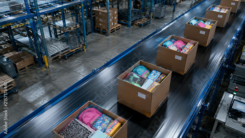 Cardboard boxes filled with school supplies moving along automated conveyor belt system in large distribution warehouse for order fulfillment and ecommerce shipping operation