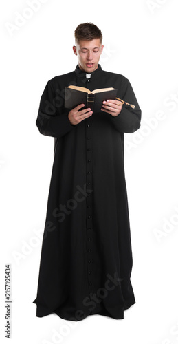 Fotografía Young priest in cassock reading Holy Bible on white background