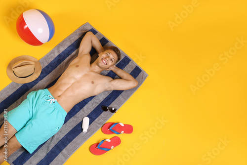 Foto Man with beach accessories sunbathing on yellow background, top view
