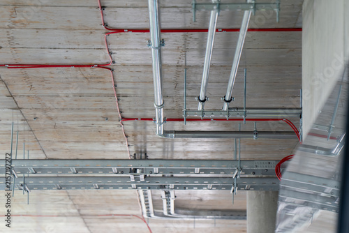 Perforated steel cable trays with fire alarm conduits and metal piping installed under concrete ceiling representing electrical MEP engineering