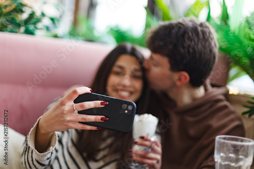 Fotografie Couple Taking a Selfie Together in a Cozy Cafe Setting with Greenery