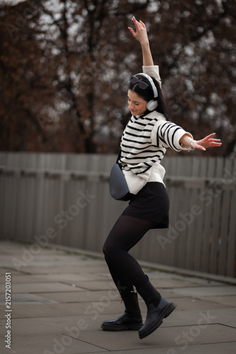 Fotografie Girl joyfully dancing outdoors in a city park while wearing headphones during a