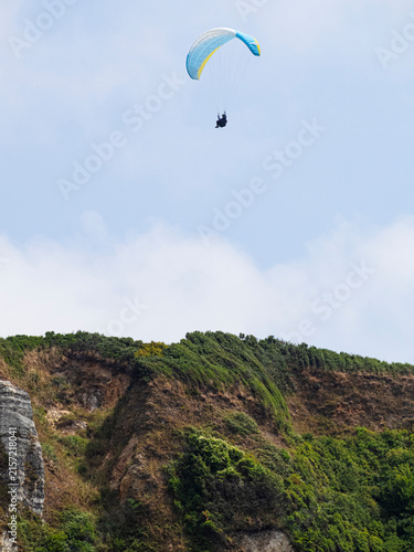 Parapentista desdendiendo del cielo azul sobre los acantilados verdes de la costa de Normandía en Francia, viajando en verano de 2022