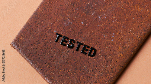 Close-up of a weathered, textured reddish-brown surface with embossed dark lettering, signifying a verification process