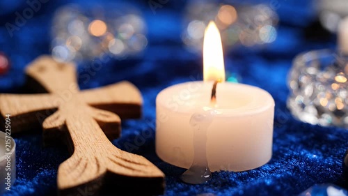 Lit candle beside wooden cross on blue background.