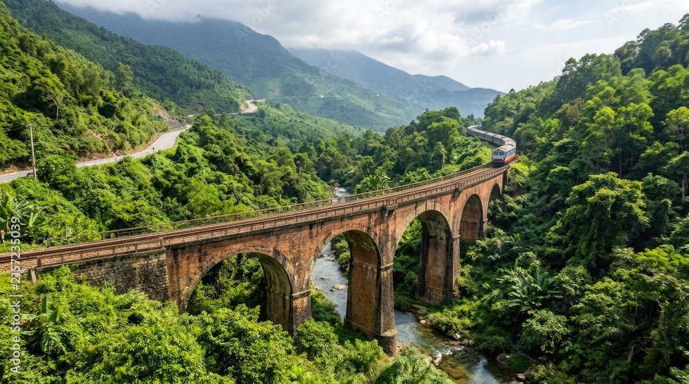 Fototapeta premium Passenger Train Crossing Historic Brick Arch Viaduct Through Lush Green Mountain Valley