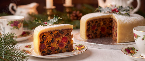 Traditional Christmas fruit cake slice with marzipan topping and holly garnish on festive table.