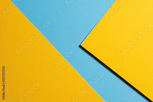 Geometric background featuring overlapping blue and yellow paper shapes creating minimalist aesthetic with shadow depth.