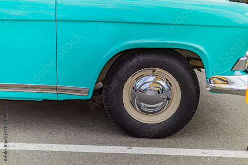 Close-up view of vintage car wheel and fender, emphasizing classic design, vibrant teal turquoise paint, contrasting white tires, reflective chrome hubcap, smooth curved fender, polished appearance