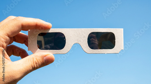 Hand holding eclipse glasses against a clear blue sky