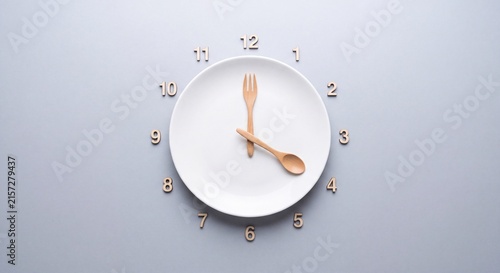 Intermittent fasting and meal timing concept featuring an empty white plate styled as a clock with wooden cutlery on grey background