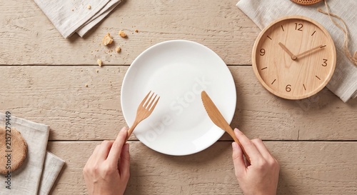 Intermittent fasting and diet timing concept featuring hands holding wooden cutlery over an empty white plate next to a clock