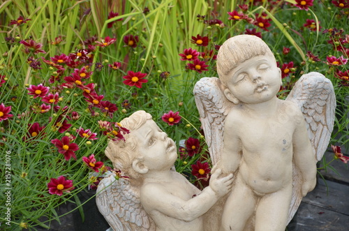Two little stone angel cherubs in flower garden