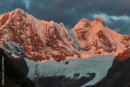 Cuadro en lienzo The towering faces of Rondoy and Jirishanca ablaze in deep orange and pink against a brooding, storm-streaked sky