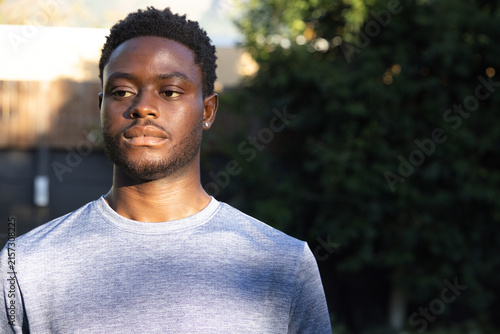 Photography African American man in 20s standing by backyard fence wearing gray tee, stud ea