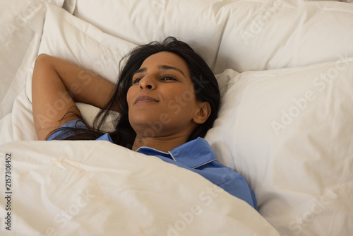 Bild auf Leinwand Indian woman reclining on bed at home, wearing light blue pajama top and covered