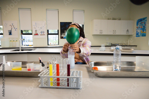 African American youth sitting school lab holding green balloon on clear bottle near test tube rack