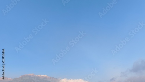 Clear blue sky above distant mountain peak and soft clouds with ample copy space for background and creative design