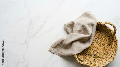 Wicker basket with beige linen napkin on white marble background, top view, perfect for food styling, culinary content and kitchen interior design
