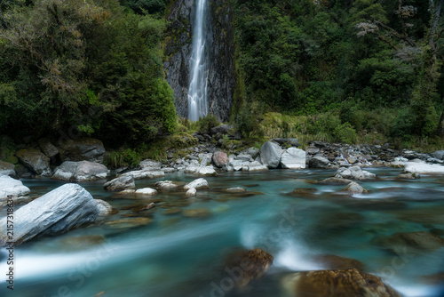 Crystal clear mountain water cascading down the cliff into the turquoise water in the Haast river