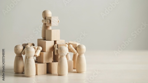 Wooden figures building a pyramid of blocks, symbolizing teamwork and collaboration.
