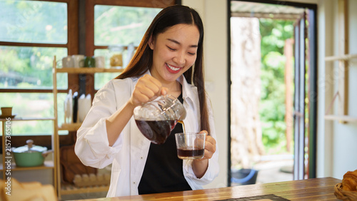 Young Asian woman pouring freshly brewed coffee into a cup in her home kitchen.