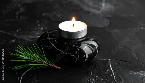 Black candle holder with lit tealight and pine branch creating quiet Christmas still life on textured dark stone surface Christmas Concept