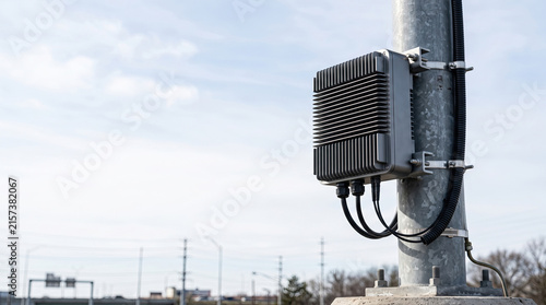 Outdoor telecom equipment enclosure mounted on metal pole against blue sky