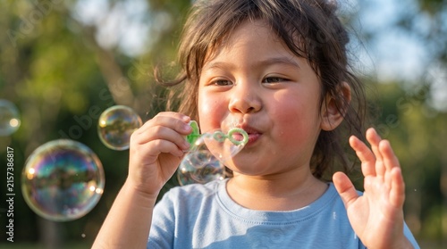 Adorable young child blowing iridescent soap bubbles in a sunlit park during a playful outdoor summer afternoon activity