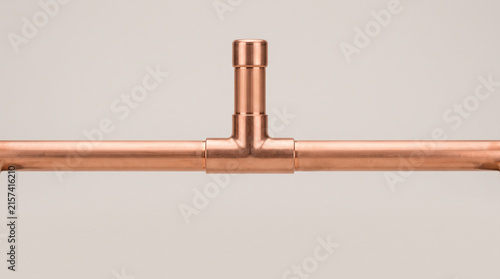 A copper pipe T-junction with a short branch line, smooth even exterior surface on all fittings, no visible marks, on a plain grey studio background, close-up product shot.