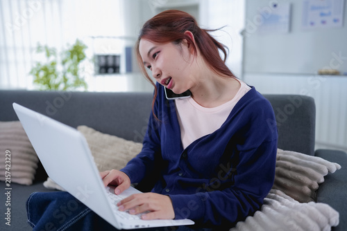 Canvastavla Young Asian woman multitasking on phone call while typing on laptop working from
