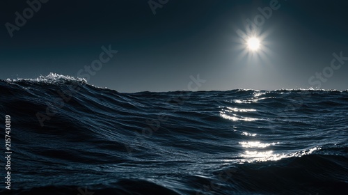 Sun glints on deep blue ocean waves under a clear, dark sky