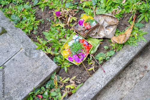 Top view of traditional Balinese Canang Sari offering with colorful flowers and incense on grass.