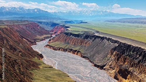 Aerial view of a winding braided river flowing through a deep rocky canyon under a clear blue sky in Anjihai Grand Canyon, Xinjiang, China