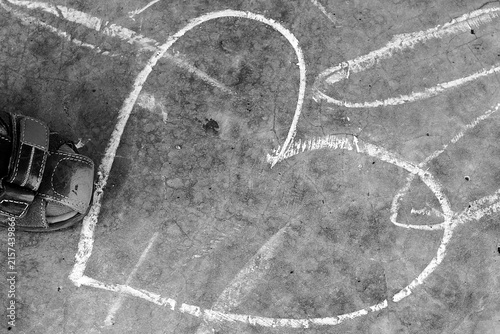 Black and white image of a child’s sandal beside large chalk drawings on pavement, capturing creative outdoor play and childhood imagination.