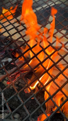 Flames poking through the gaps on a grill. 