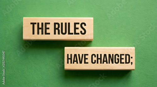 Two wooden blocks with bold black text reading THE RULES and HAVE CHANGED placed on a solid bright green background, casting subtle shadows for a clean, modern look featuring wood blocks and message