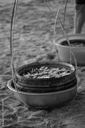 Quadro su tela Black and white photograph of fresh fish baskets on a shoulder pole on the sandy