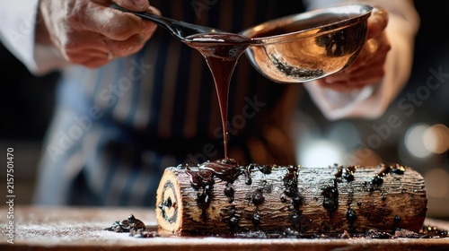 A dynamic culinary shot of a chef pouring a glossy, dark chocolate sauce over a Yule log cake