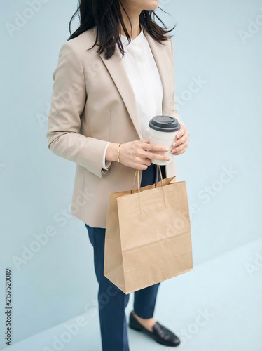 Businesswoman holding coffee cup and paper bag against light blue wall