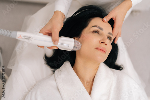Closeup top view of relaxed adult woman receiving innovative rf microneedling facelift procedure from skilled esthetician, modern hardware cosmetology method for skin tightening and wrinkle reduction.