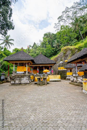 фотографія BALI, INDONESIA – OCTOBER 20, 2024: Traditional thatched-roof Hindu shrines draped in yellow ceremonial cloths at Gunung Kawi Temple