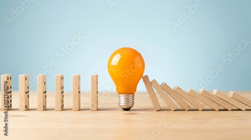 Yellow light bulb stopping a row of falling wooden dominoes on a wooden table surface