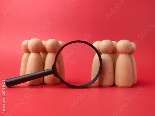 A black magnifying glass rests between two distinct groups of wooden peg figures on a red background
